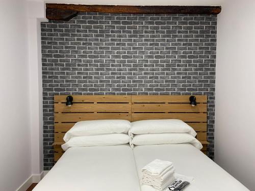 a bed with white pillows and a brick wall at Casual Mardones in Bilbao