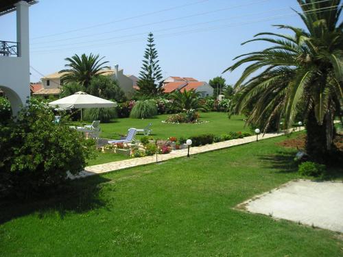 een tuin met ligstoelen, een parasol en palmbomen bij Eleftheria Studios and Apartments in Acharavi
