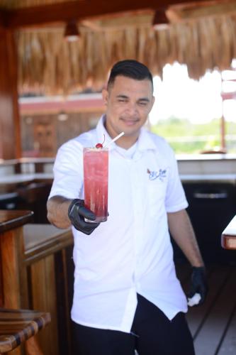 a man in a kitchen holding a red drink at El Ben Cabañas in Caye Caulker