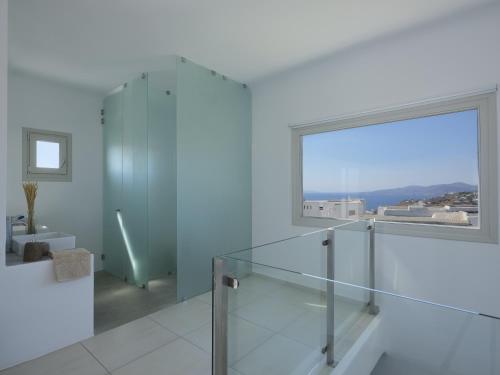 La salle de bains blanche est pourvue d'une douche en verre et d'une grande fenêtre. dans l'établissement Secret Island, à Tourlos