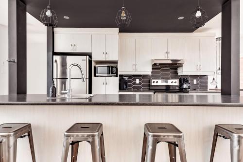 a kitchen with white cabinets and a counter with stools at 25- Chalet à Louer à Stoneham in Stoneham