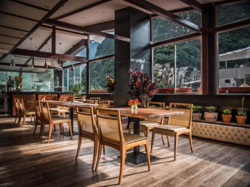 un restaurante con mesas y sillas de madera y ventanas grandes en Jaya Machu Picchu Boutique Hotel, en Machu Picchu