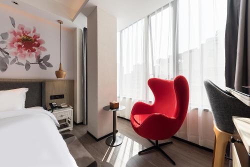 a red chair in a room with a bed and a window at Paco Hotel Canton Tower Pazhou-Free shuttle bus for canton fair in Guangzhou