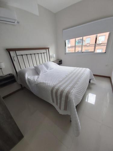 a white bedroom with a bed with a striped blanket at Moreno Apart in San Miguel de Tucumán