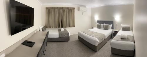 a hotel room with two beds and a flat screen tv at Rocky Gardens Motor Inn Rockhampton in Rockhampton