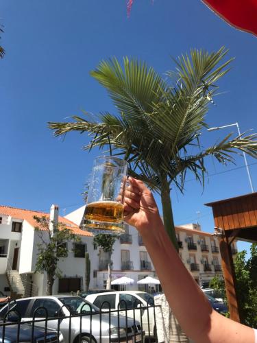 a person holding a glass of beer in front of a palm tree at casa de piedra.The stone house in Turre
