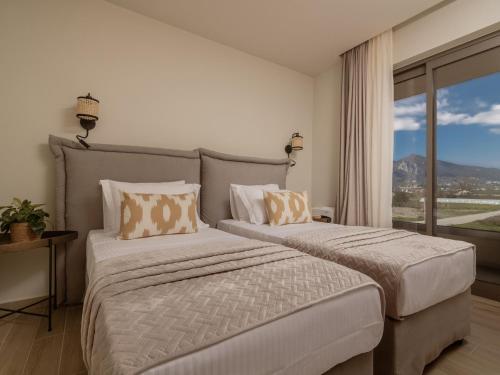 two beds in a hotel room with a window at Chrysothemis Villas in Pigadhákia