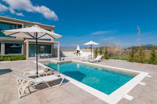 a pool with chairs and an umbrella next to a house at Chrysothemis Villas in Pigadhákia