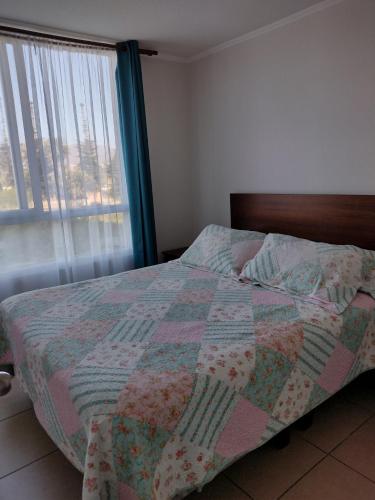 1 dormitorio con 1 cama con edredón y ventana en Departamento Coquimbo a pasos de la playa, en Coquimbo