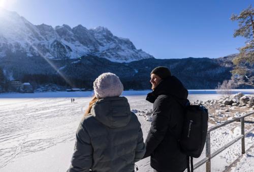two people standing next to a fence looking at a lake at Eibsee Hotel in Grainau