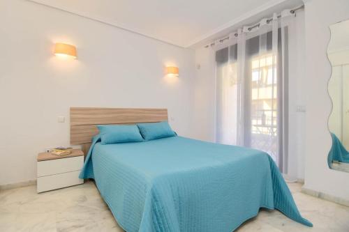 a white bedroom with a blue bed and a window at Marjeleta Apartamento in Moraira
