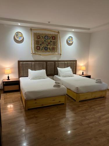 two beds in a room with two lamps on the wall at Lyabi House Hotel in Bukhara