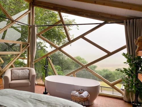 ein Schlafzimmer mit einer Badewanne vor einem großen Fenster in der Unterkunft Quaint Luxury Villas in Graskop
