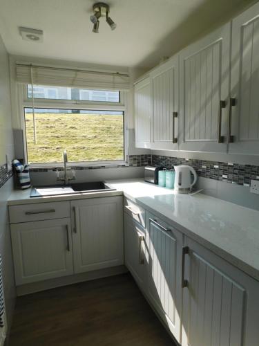 a kitchen with white cabinets and a sink and a window at 238 Norton Park, Dartmouth 2 bed holiday home with free parking in Dartmouth