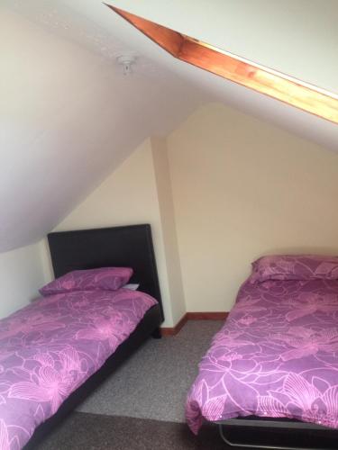 two beds in a room with purple sheets at Honeycomb Cottage in Aberdare