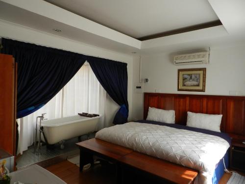 a bedroom with a bed and a bath tub next to a window at Sleepers Villa Guesthouse in Polokwane