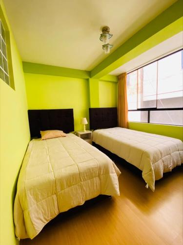 two beds in a room with green walls and a window at Departamento Los Manantiales Cusco in Cusco