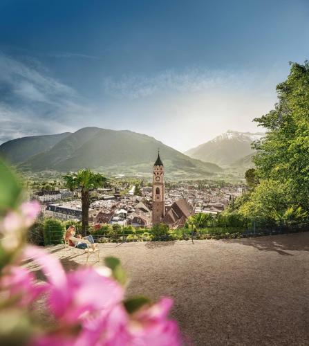 a woman sitting on a bench looking at a city with a clock tower at Genusshotel Diamant in Naturno