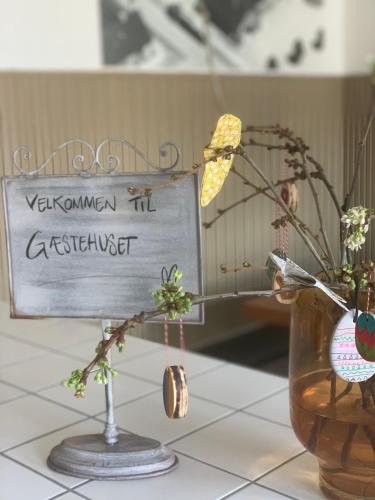 a sign on a table with flowers and a vase at GÆSTEHUSET in Tarm