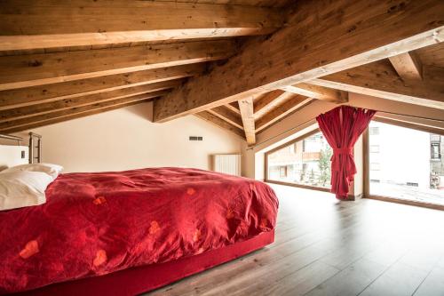 Un dormitorio con una cama roja en una habitación con techos de madera. en Esprit Carrel, en Valtournenche