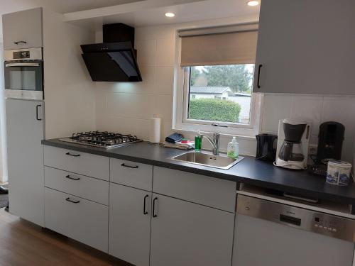 a kitchen with white cabinets and a sink and a window at Modern en chic chalet tot 4 personen op de Veluwe Recreatiepark De Oude Driest - All inclusive in Putten