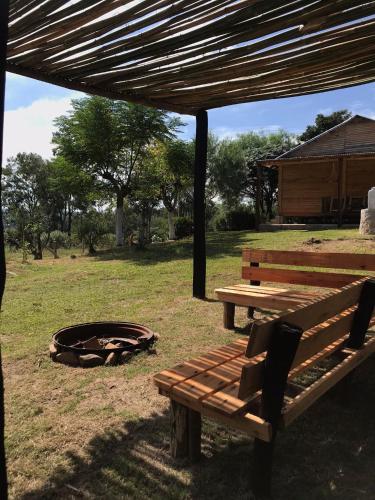two wooden benches sitting under a pavilion in a field at Cabaña Los Nietitos in Tranqueras