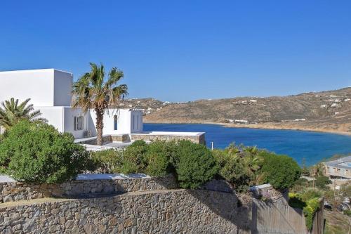 a white house with a palm tree and a wall at Mykonian house in Elia beach by GHH in Elia Beach