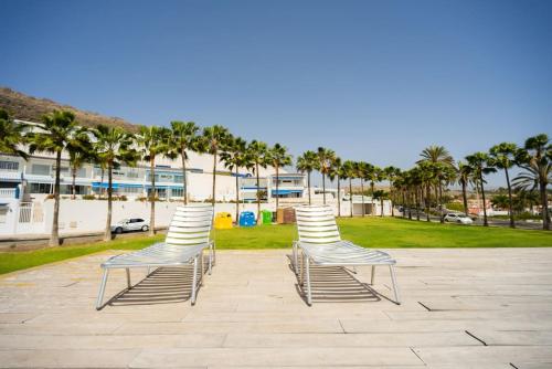 una fila de sillas sentadas en un patio con palmeras en FABULOUS BUNGALOW , WIFI, SWIMMING POOL AND BEACH en Pasito Blanco