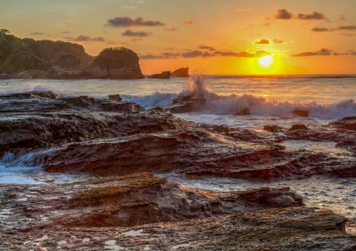 a sunset on the beach with rocks in the ocean at Casas Kismet in Nosara