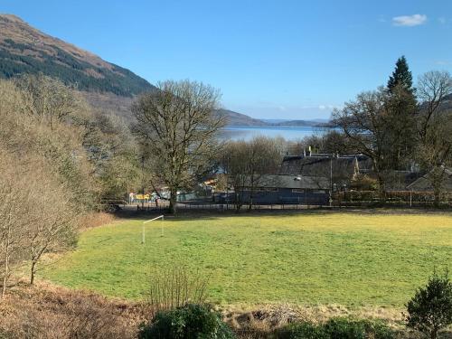 a field of grass with a lake in the background at Glebe Country House Tarbet in Arrochar