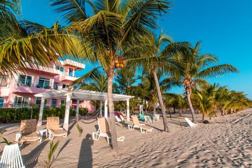 a beach with chairs and palm trees and a pink building at Miramar Suites in Placencia