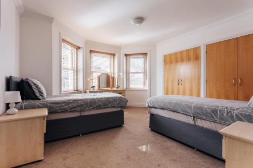 a bedroom with two beds and cabinets and windows at Top quality beach front apartment sleep up to 7 guests in Bournemouth