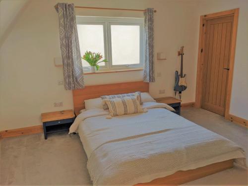 a bedroom with a large bed and a window at Cranmer - New Eco Beach House 4 Bed HOT TUB & Bikes in Camber
