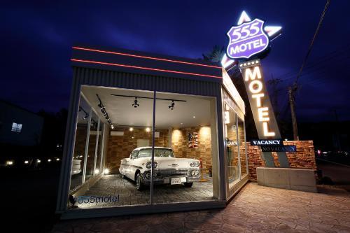an old car sits inside of a building with a neon sign at 555 MOTEL GOTEMBA in Gotemba