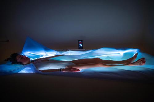 a woman laying on a bed under a blue light at Paradiso Pure Living Vegan Hotel in Alpe di Siusi