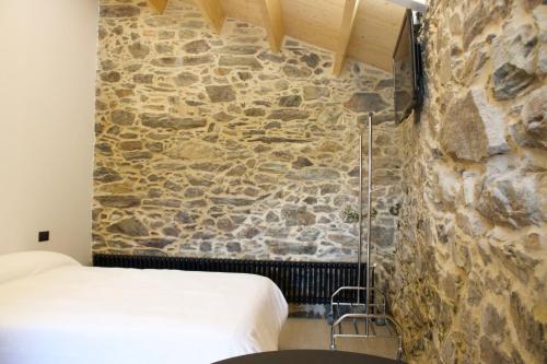 1 dormitorio con pared de piedra junto a la cama en O lar de San Fins-Casita rural, en A Coruña