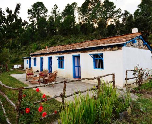 a small white house with blue doors and chairs at Thikalna Himalayan Retreat in Almora