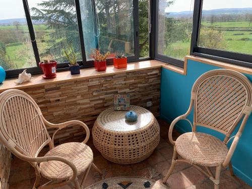 two chairs and a table in a room with windows at L’En Vert du Monde in Saint-Boil