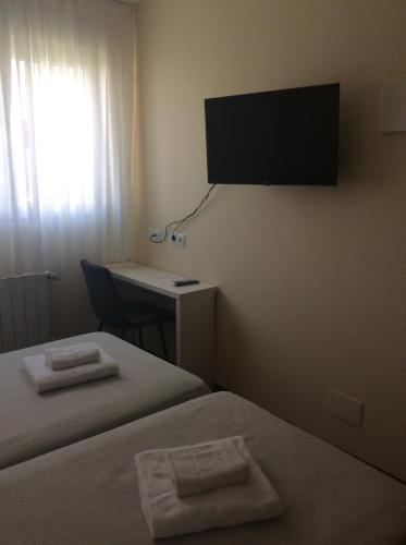 a room with two beds and a desk and a television at Posada H.El Alba in Boó de Piélagos
