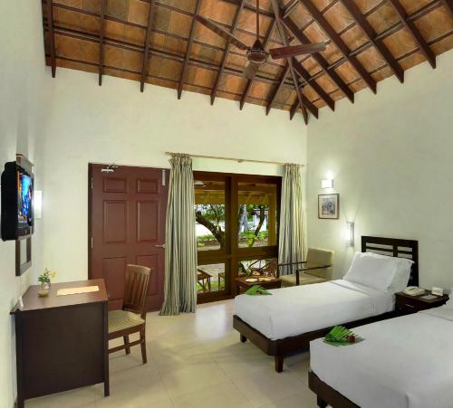 a bedroom with two beds and a desk and a television at Abad Turtle Beach in Mararikulam