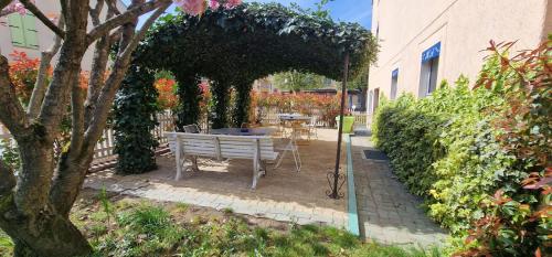 a white bench sitting under a pergola in a garden at Kyriad Direct Arpajon in Arpajon