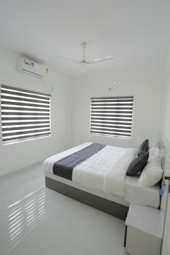 a white bedroom with a bed and two windows at Yelza Hotel and Residence in Alwaye