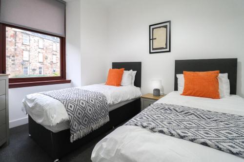 two beds with orange pillows in a room at Sonas Apartment Greenock in Greenock
