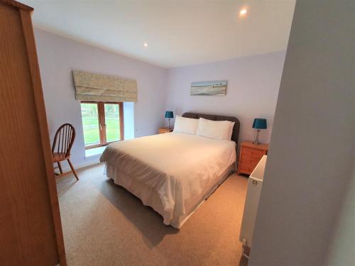 a bedroom with a bed and a chair and a window at Fodol Cottages in Menai Bridge