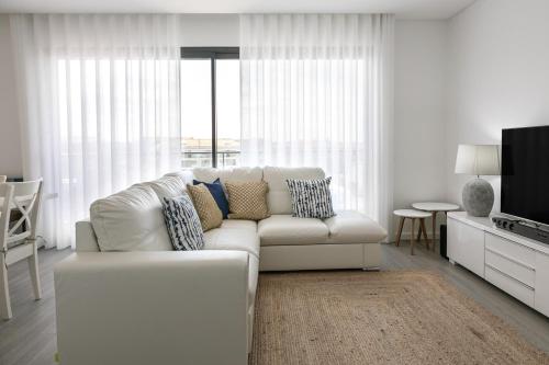 a white living room with a white couch and a tv at Consolação Supertubos Beach Apartment in Consolação