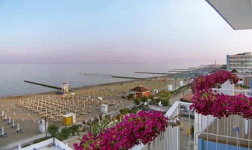 a beach with rows of tables and chairs and pink flowers at Hotel Condor in Lido di Jesolo
