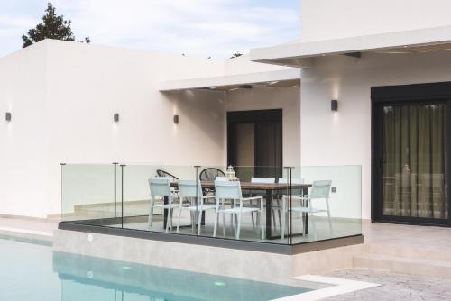 a house with a glass table and chairs next to a swimming pool at Villa De Reve in Laganas