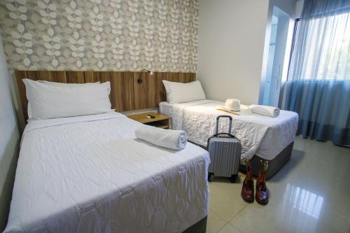 a hotel room with two beds and a suitcase at Hotel Horto in Rondonópolis