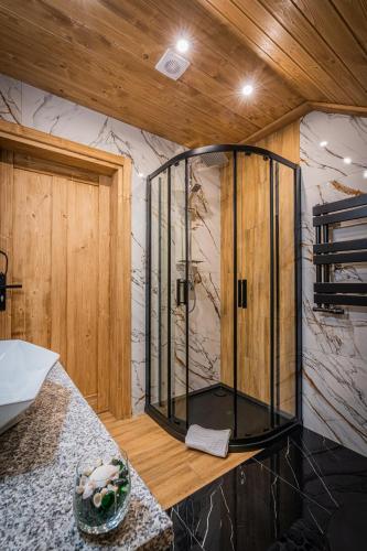 a glass shower in a room with a wooden wall at Dworek nad Jałowcami z Jacuzzi in Biały Dunajec