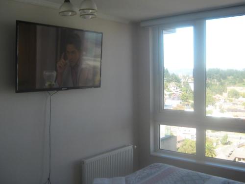 a bedroom with a television and a window with a person on a cell phone at Departamento Parque Urbano 1710 in Concepción
